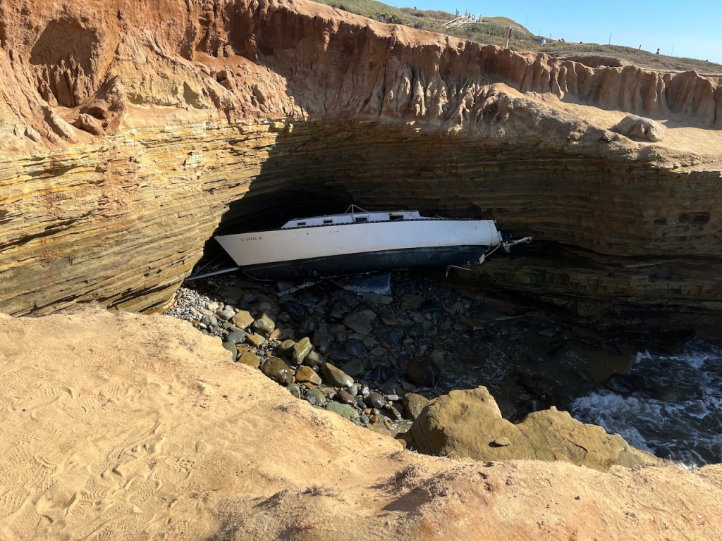 White boat stuck under rocky cliffs at the ocean.